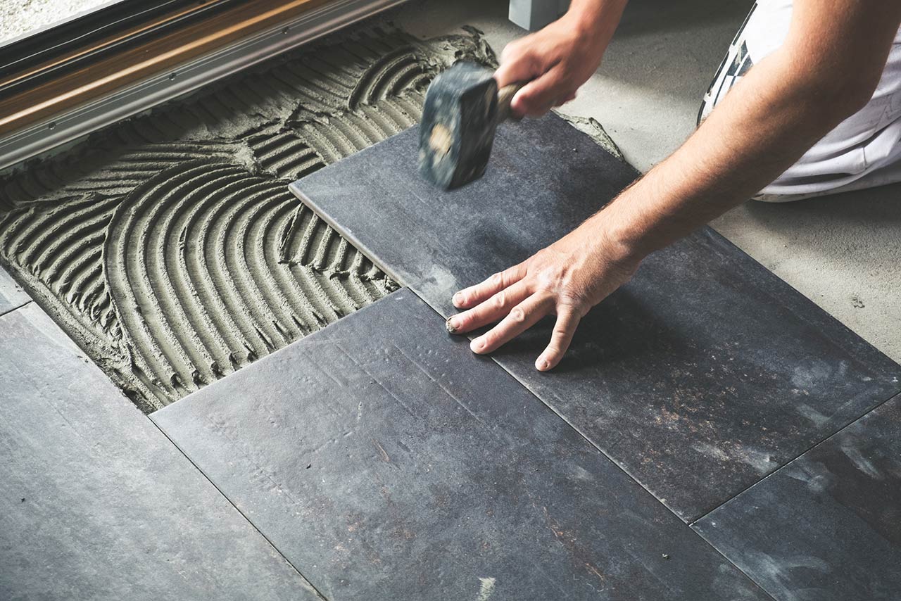 Photo of a worker carefully placing ceramic floor tiles on adhesive surface