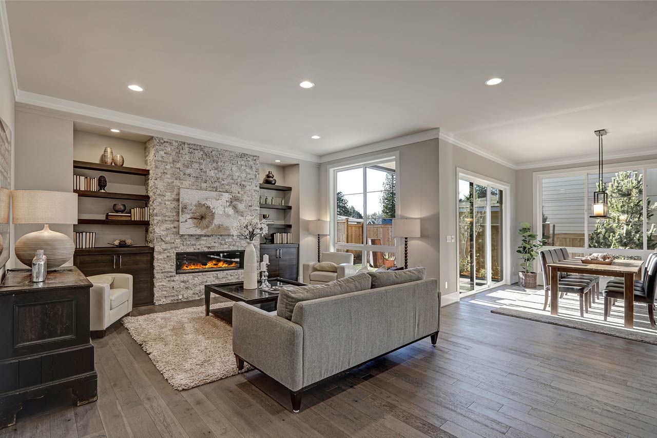 Living room interior in gray and brown colors features gray sofa atop dark hardwood floors facing stone fireplace with built-in shelves