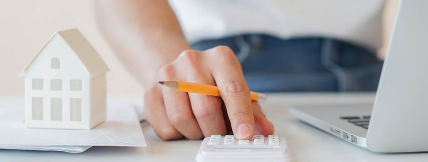 Close up of a mans hand with a pencil calculating with a small home model