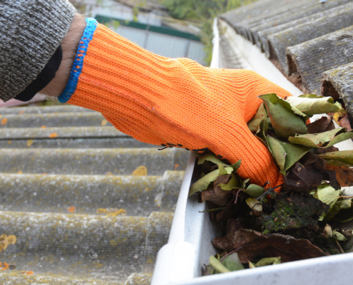 Roofer cleaning a rain gutter with an orange glove on