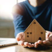 Hands holding a wooden model home with an open laptop