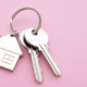 Silver house key with house keychain on pink background