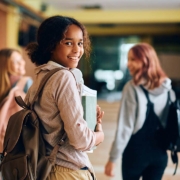 Happy African American high school student walking through hallway with her friends and looking at camera