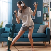 Cheerful woman cleaning up her home and singing, using the vacuum cleaner as a microphone