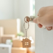 A key inserted into a door of the new house with a hand opening it, inside the room are cardboard boxes and furniture