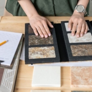 Hands of designer on samples of marble tile surrounded by wallpaper patterns during work over new project or order of client