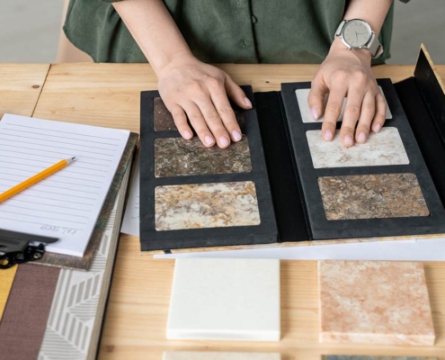 Hands of designer on samples of marble tile surrounded by wallpaper patterns during work over new project or order of client