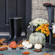 Traditional style front porch decorated for autumn with rain boots, heirloom gourds, white pumpkins, mums and rocking chair