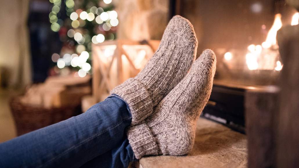 Feet of unrecognizable woman in woollen socks by the Christmas fireplace