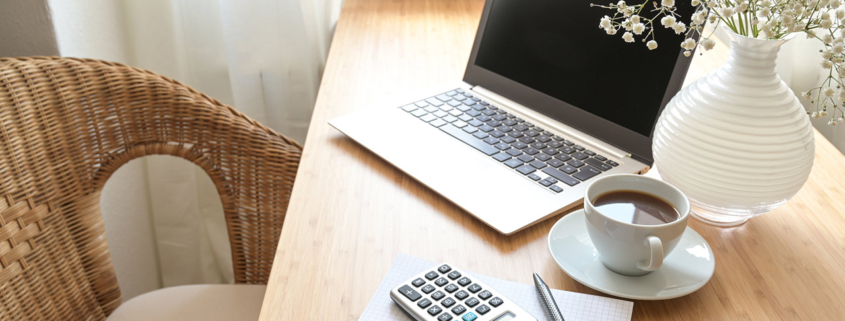 Home office desk with laptop computer, calculator, spiral book, coffee and a white flower bouquet, business accounting concept, copy space, selected focus